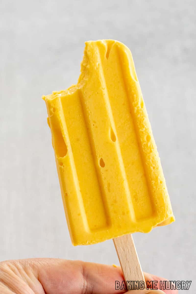 hand holding up mango popsicle