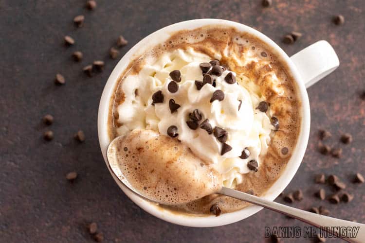 hot chocolate with chocolate chips topped with whipped cream in large mug with spoon