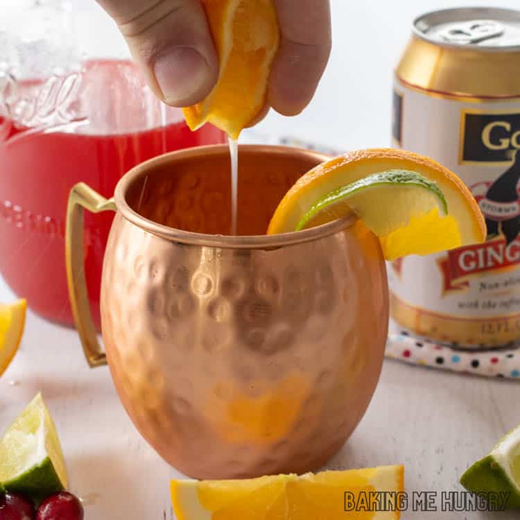 hand squeezing orange into copper mug