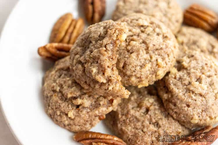 one of the brown butter pecan cookies with a bite missing on top of the plate of cookies