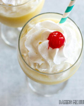 two goblets with pina colada mocktail garnished with whipped cream, cherries, and straws from overhead