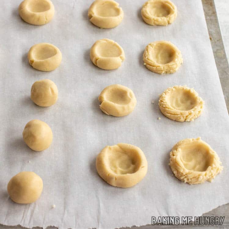 parchment with balls of dough, thumb pressed cookies, and thumbprint cookies with edges that have lines from a fork