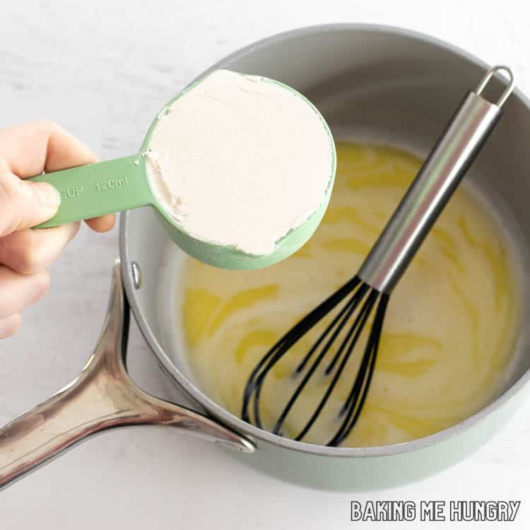 hand adding flour to small saucepan