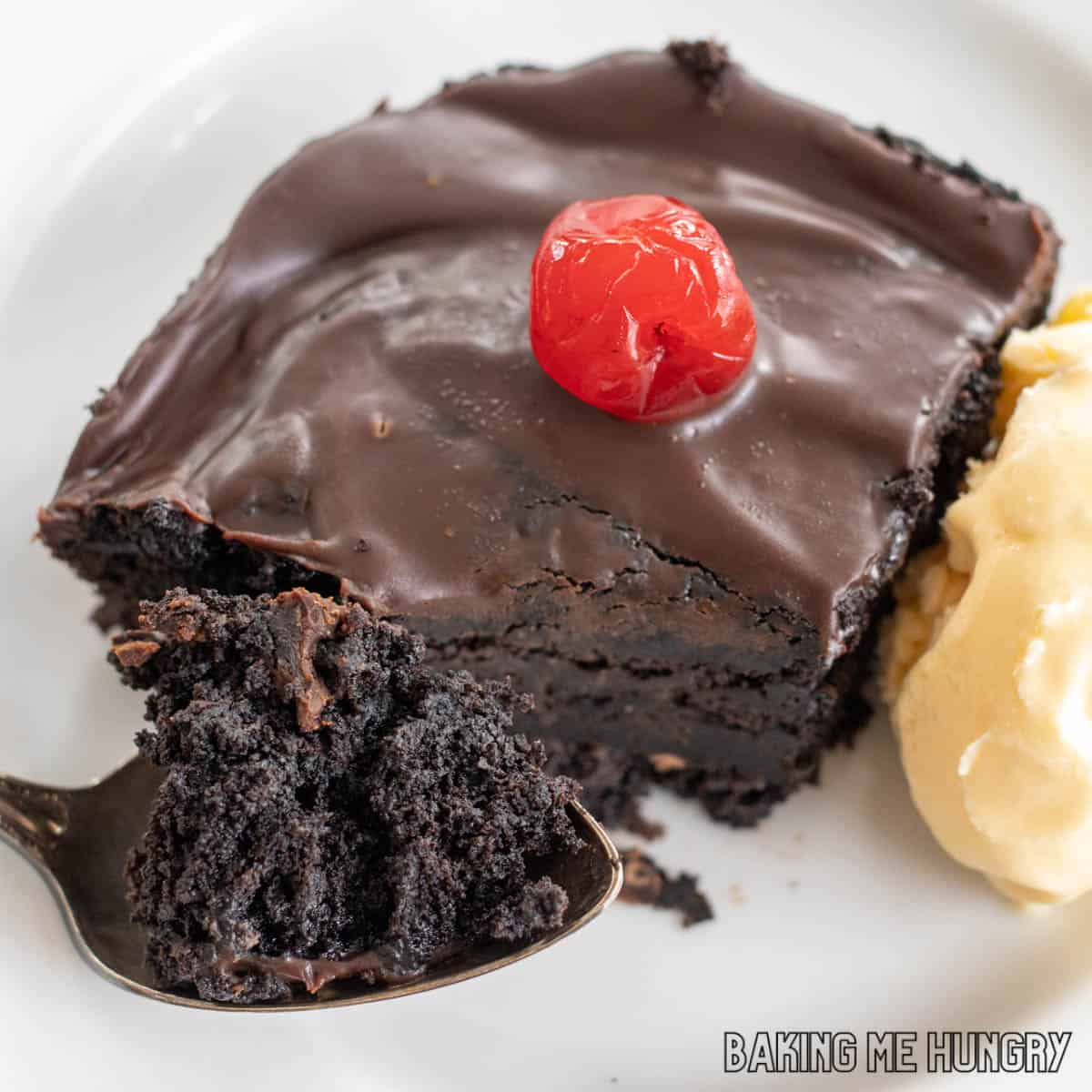 one of the chocolate cherry brownies on a plate with vanilla ice cream and bite on spoon