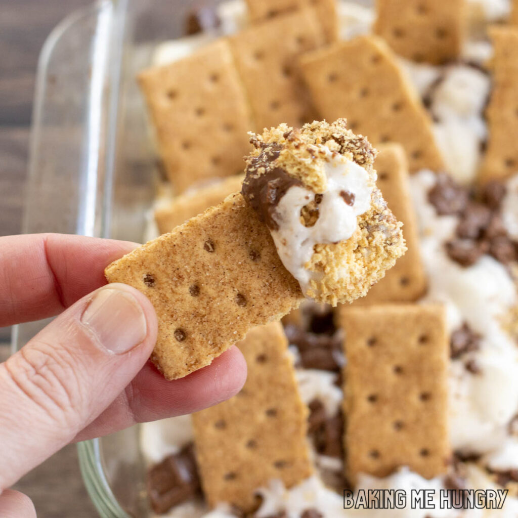 oven baked s'mores dip recipe shown scooped onto a graham cracker