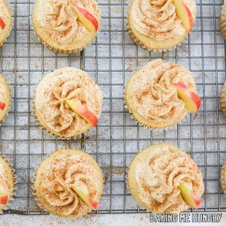 frosted apple cider cupcakes garnished with cinnamon and apple slices on wire rack close up