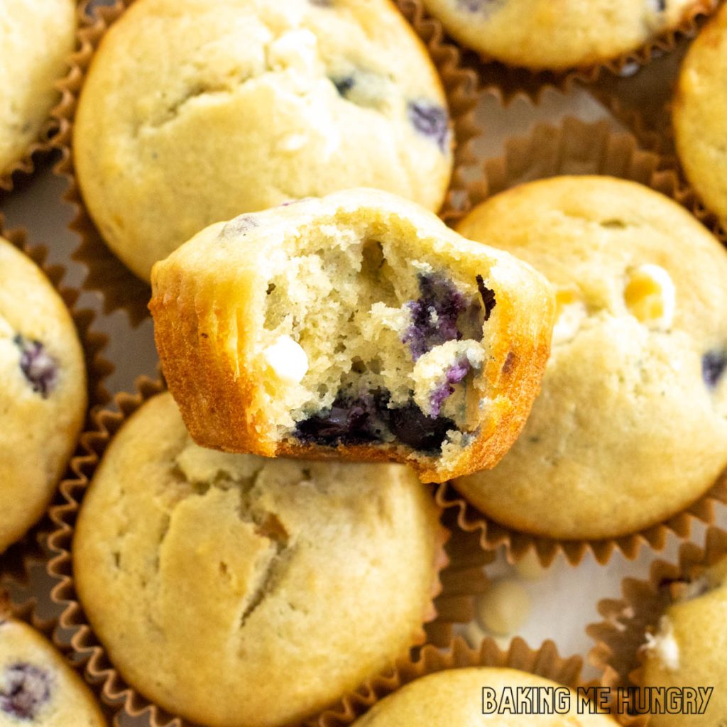 one of the blueberry white chocolate muffins missing a bite resting on other muffins