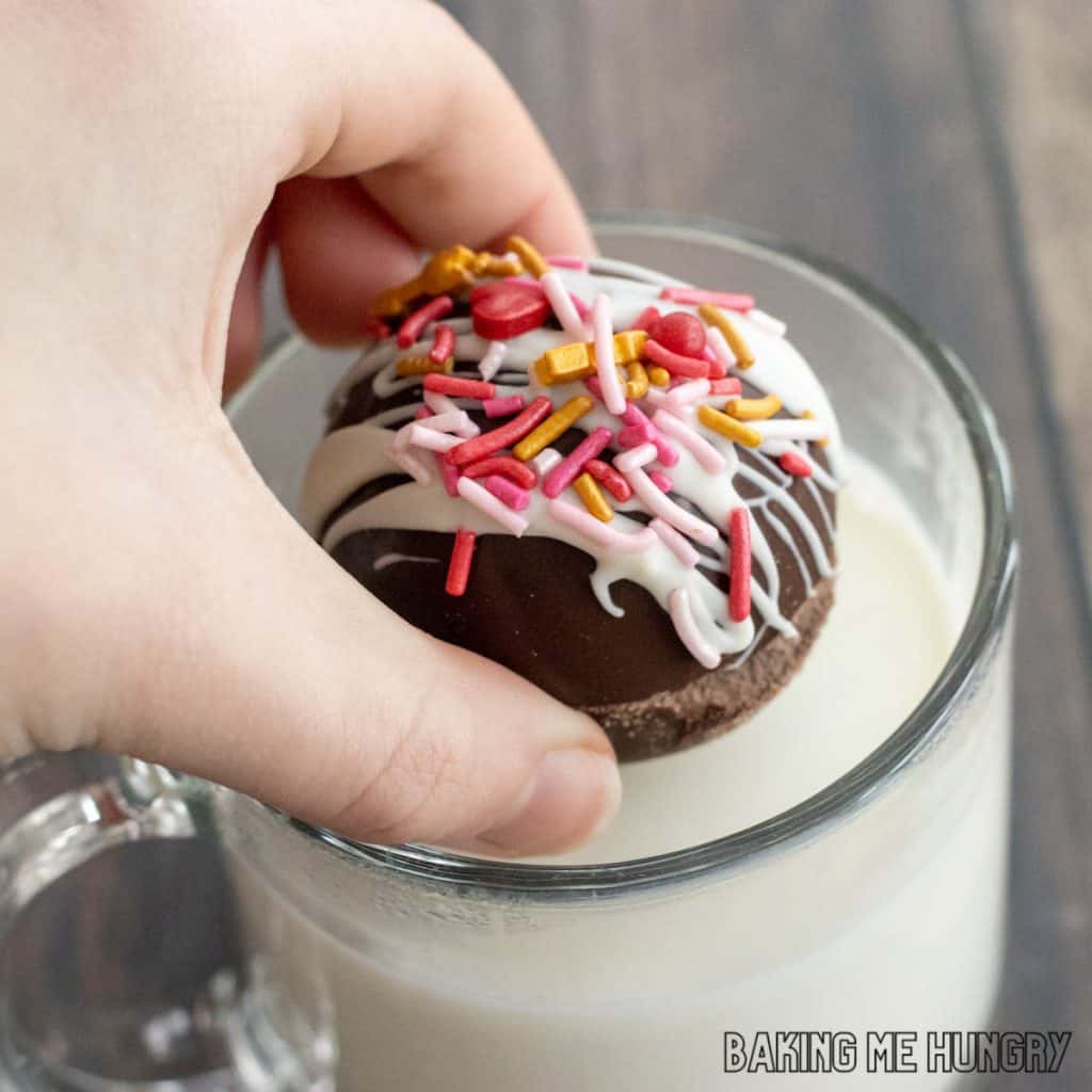 hand putting a valentine's hot chocolate bomb in a mug of milk