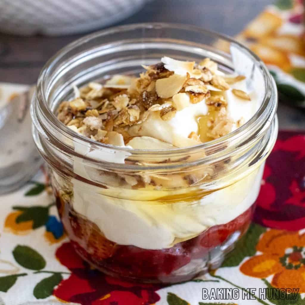 vanilla almond granola recipe on top of yogurt with honey and strawberries in small jar