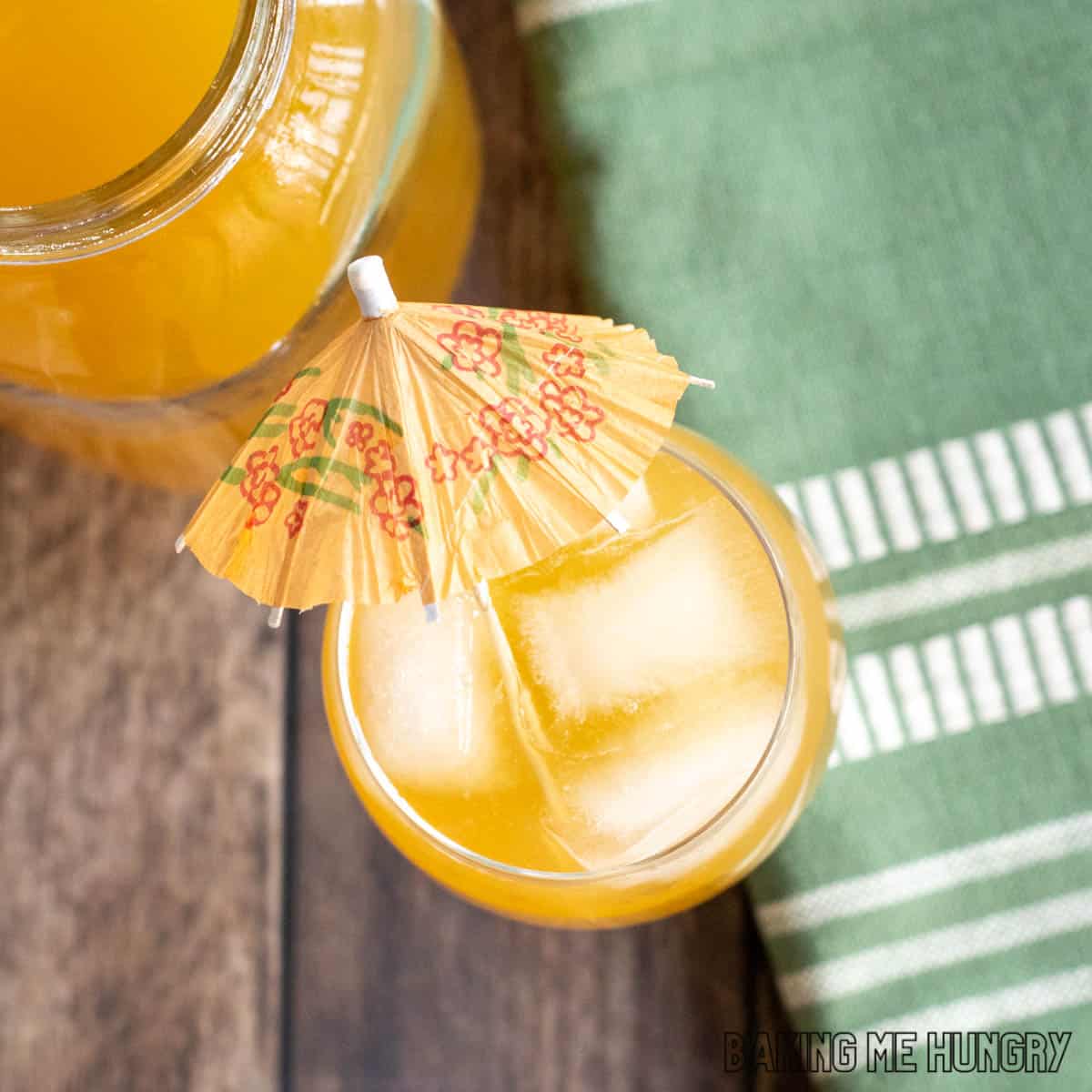 peach green tea lemonade recipe in a stemmed glass with an umbrella next to jar of tea