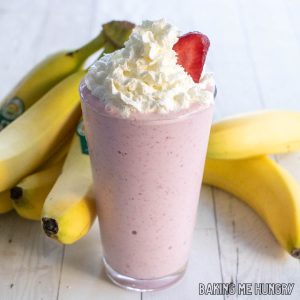 strawberry banana milkshake topped with whipped cream with bananas behind