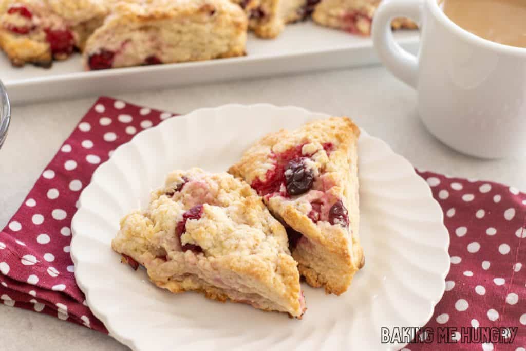 white chocolate cranberry scones with cut of coffee next to it and platter of scones behind