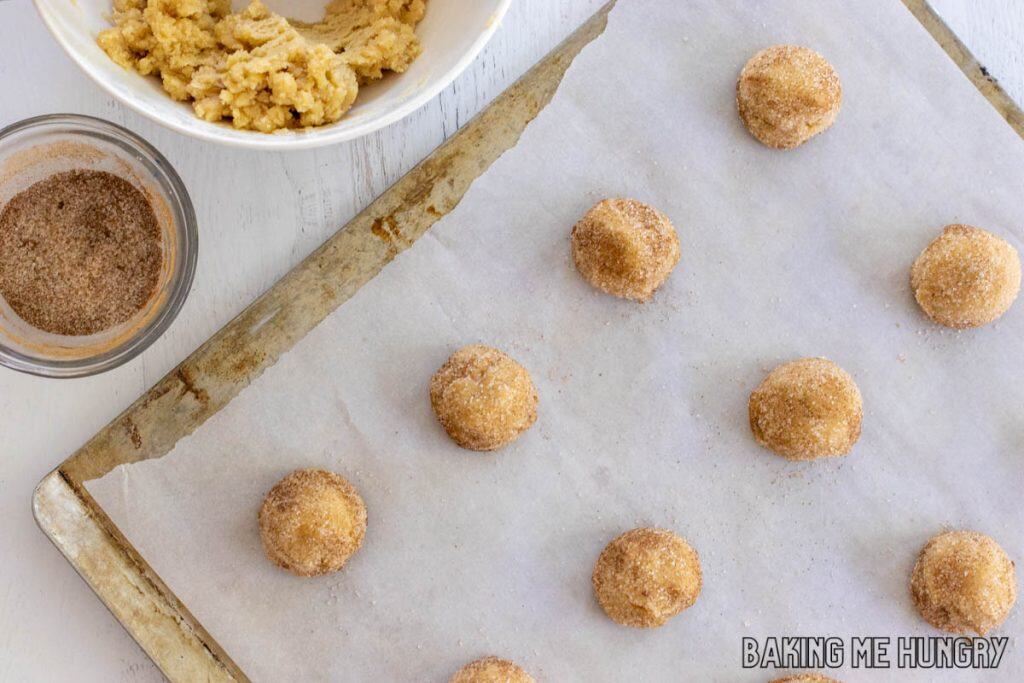 balls of dough with small bowl of cinnamon sugar and some on tray