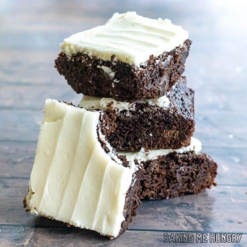 chocolate brownies with cream cheese frosting in a stack with one on its side missing a bite