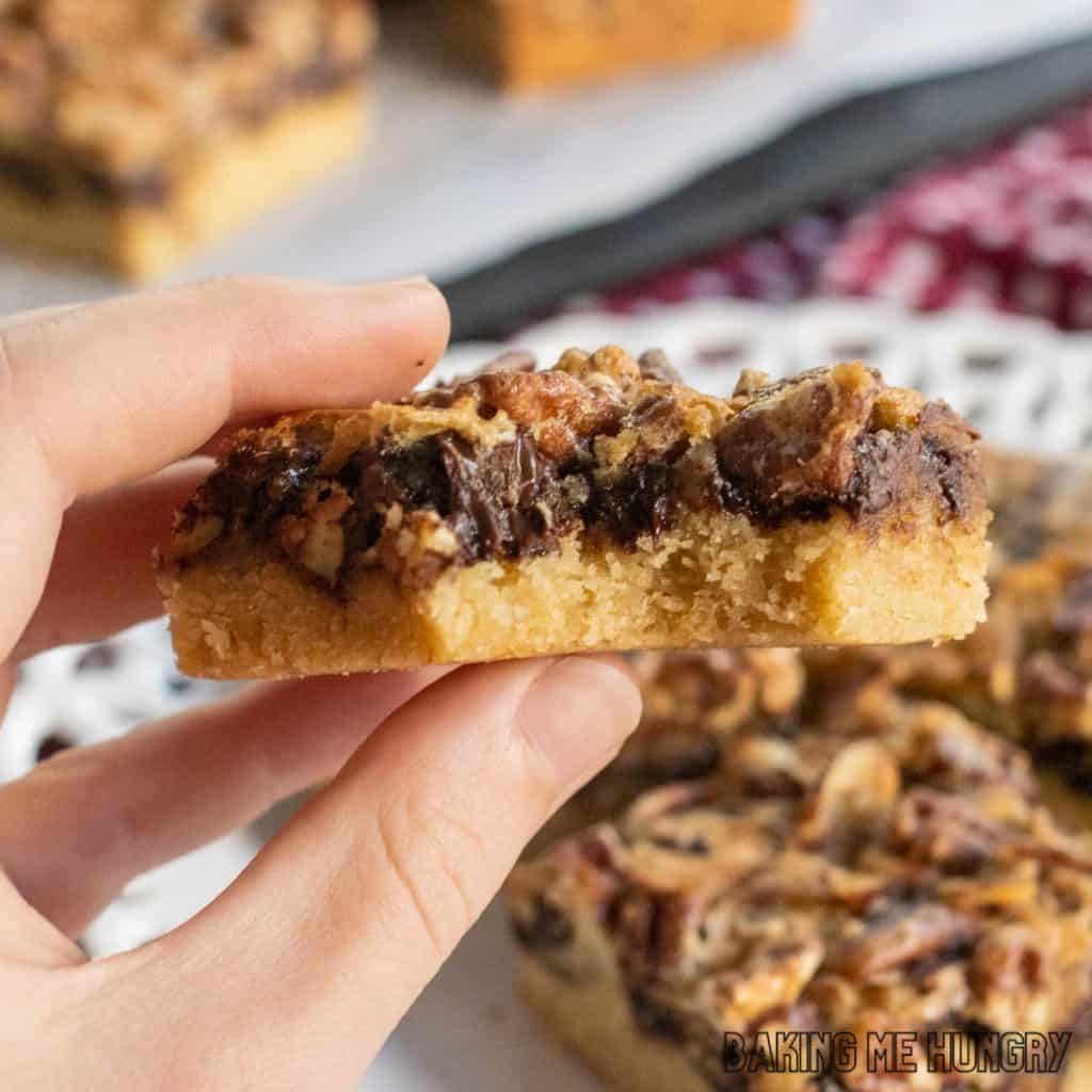 hand holding one of the chocolate pecan pie bars with a bite missing