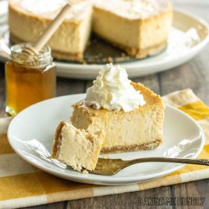 honey cheesecake recipe slice on a plate with whipped cream with whole cheesecake in background