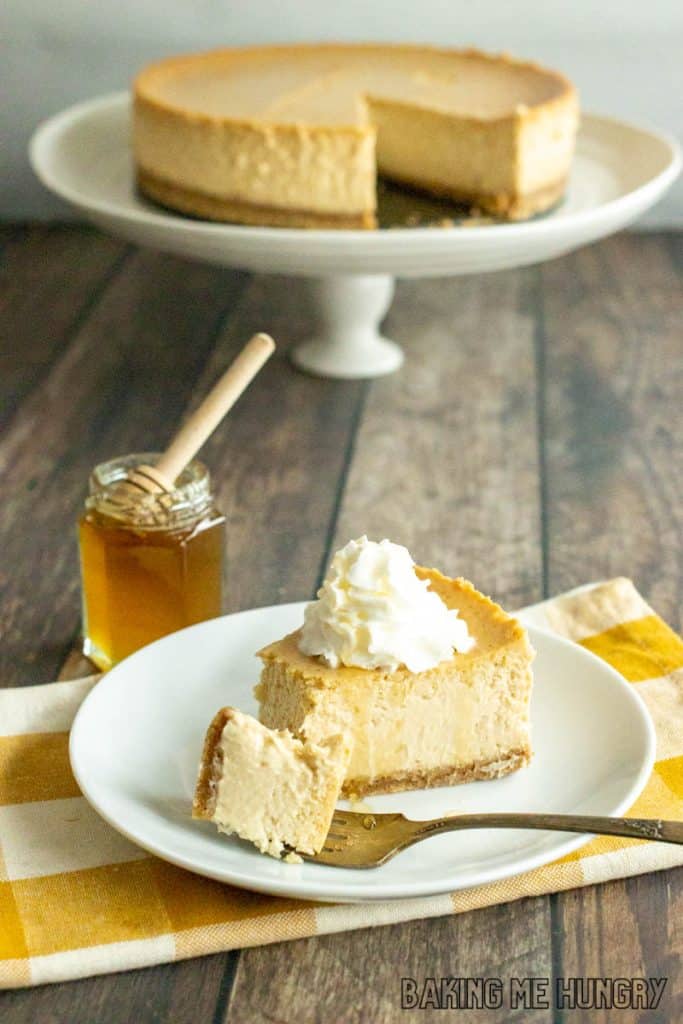honey cheesecake recipe slice on a plate with remaining cheesecake on pedestal in background