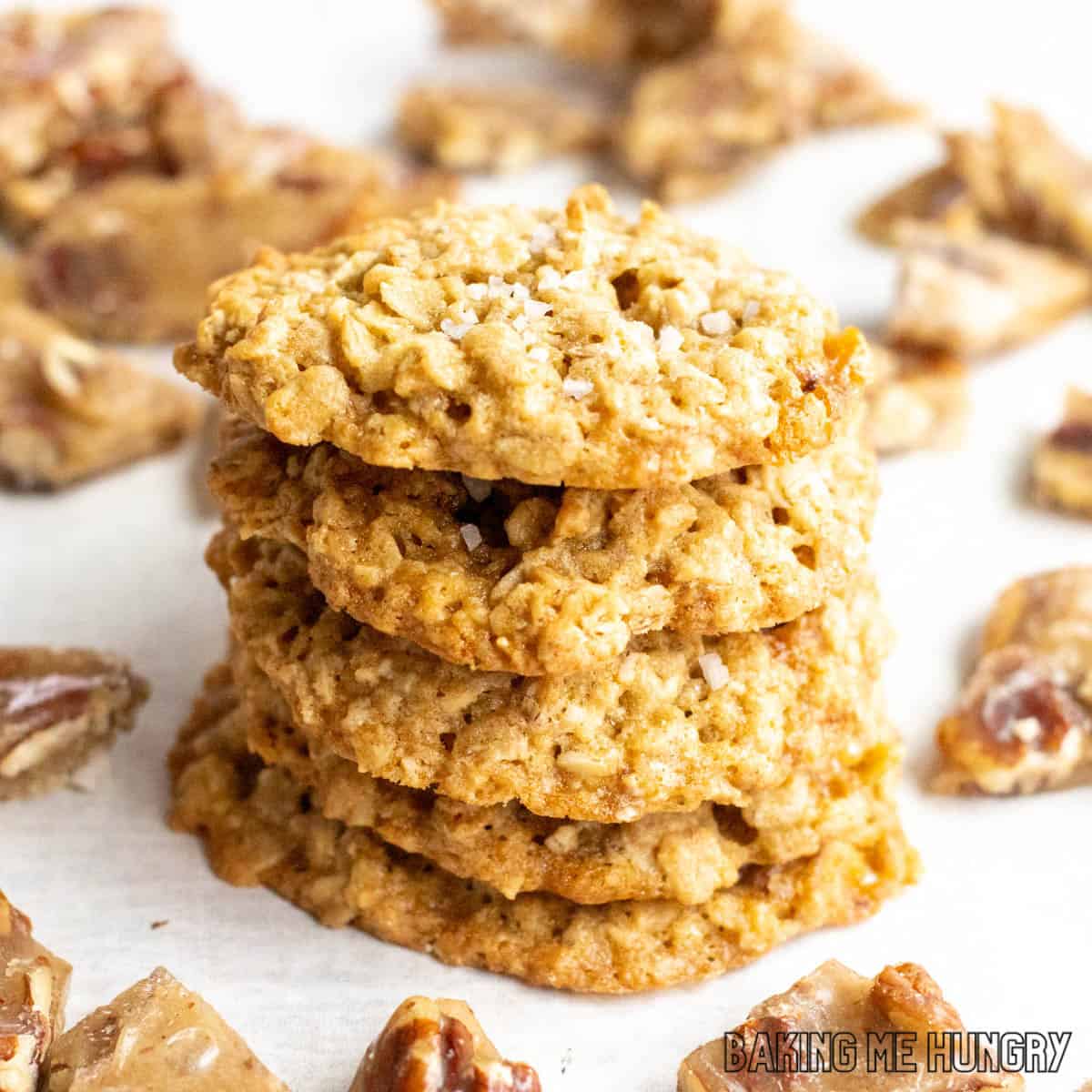 oat and pecan brittle cookies in a stack surrounded by pieces of pecan brittle