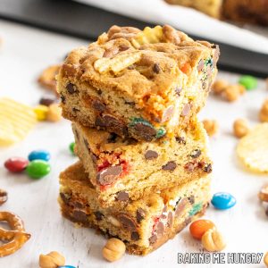 kitchen sink cookie bars recipe with potato chips, pretzels, caramel bits, m&m's, and chocolate chips shown with 3 bars in a stack