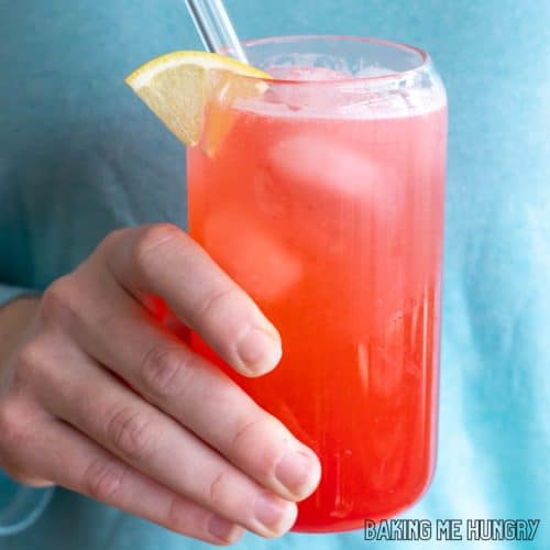 raspberry lemonade recipe in a tall glass with a lemon slice as garnish held by a hand