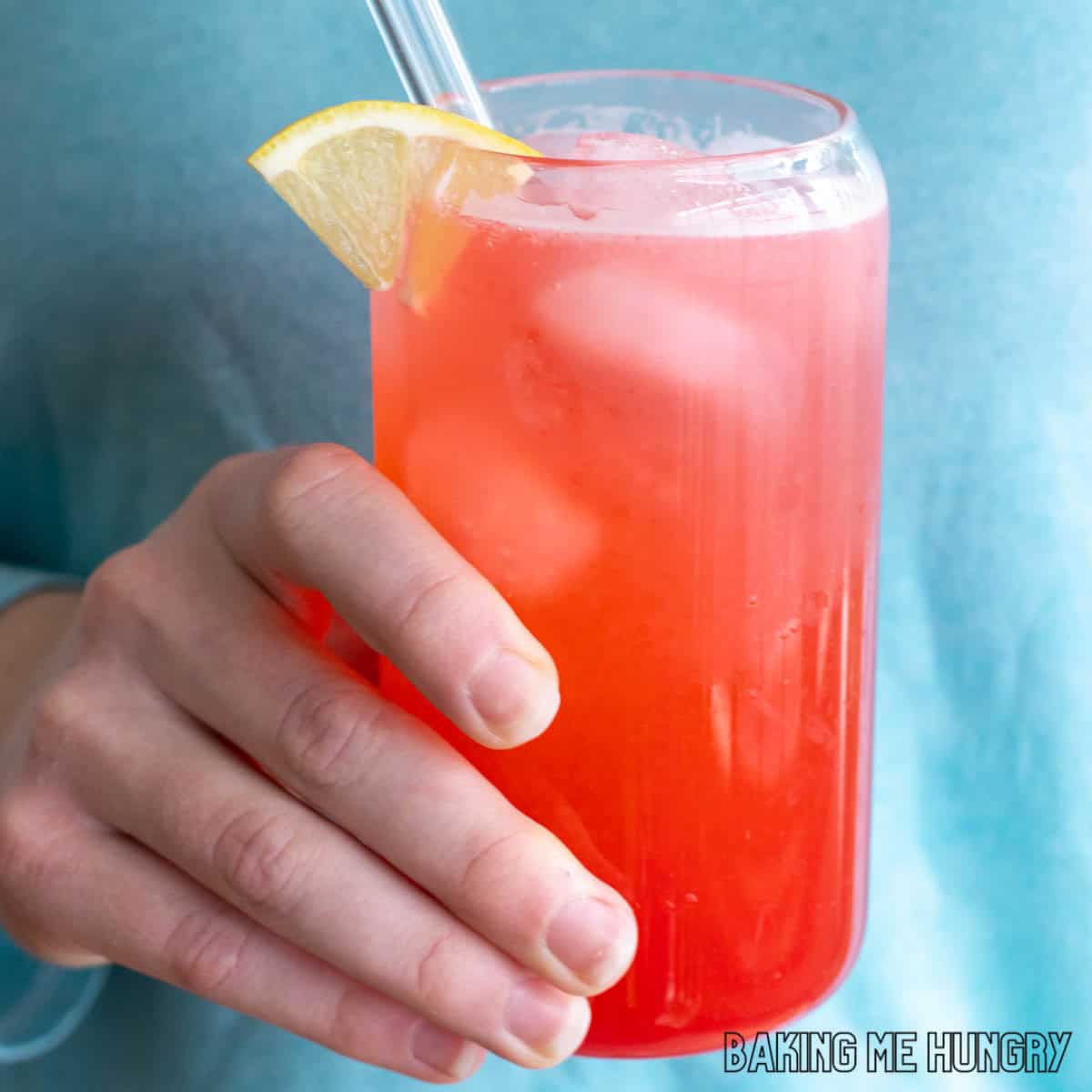 raspberry lemonade recipe in a tall glass with a lemon slice as garnish held by a hand