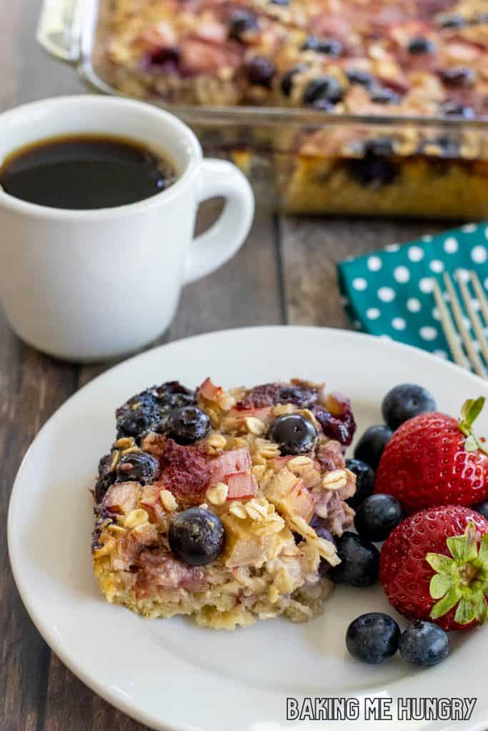slice of baked oatmeal with rhubarb and berries on a plate with baking dish behind
