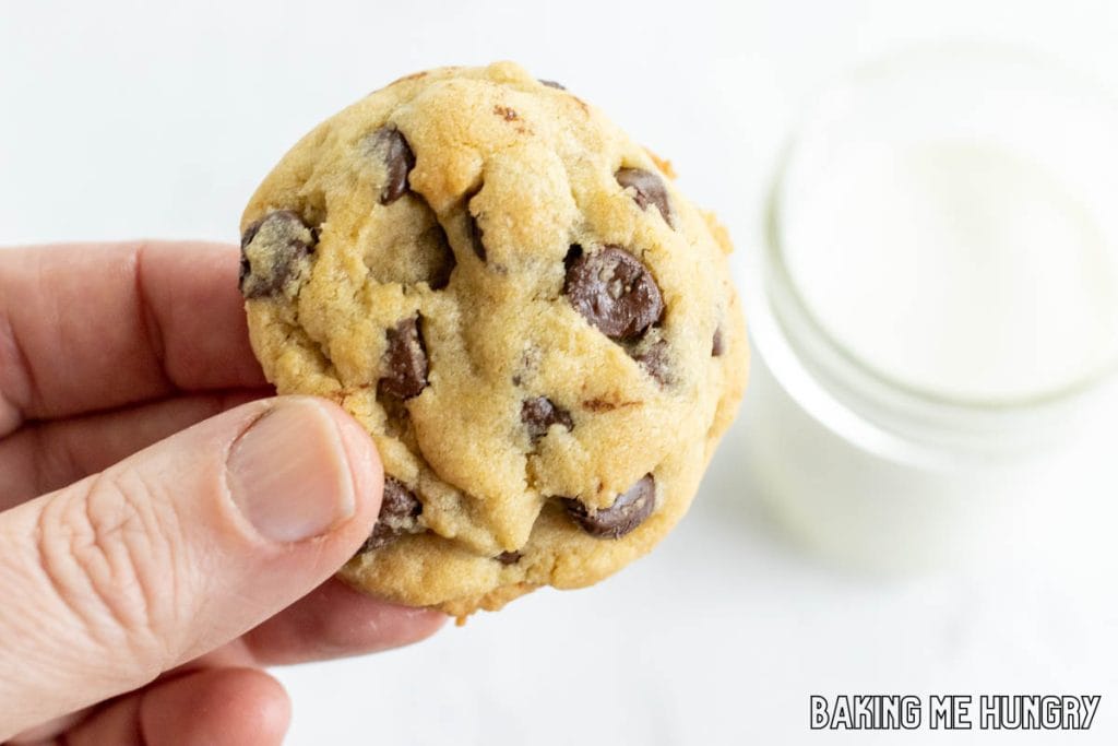 hand holding up one of the brown sugar chocolate chip cookies with a glass of milk behind