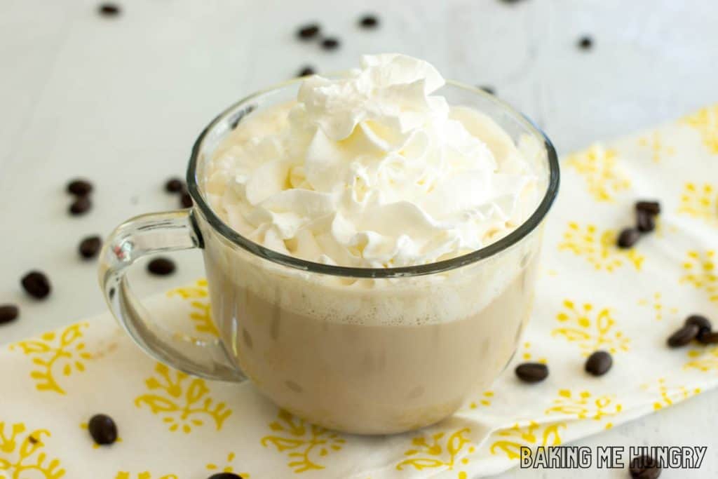 lavender latte topped with whipped cream in wide glass mug