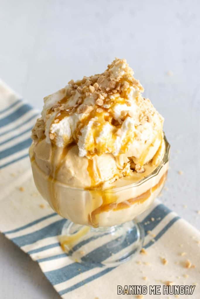 caramel crunch ice cream in a glass pedestal bowl with whipped cream, caramel syrup, and toffee bits