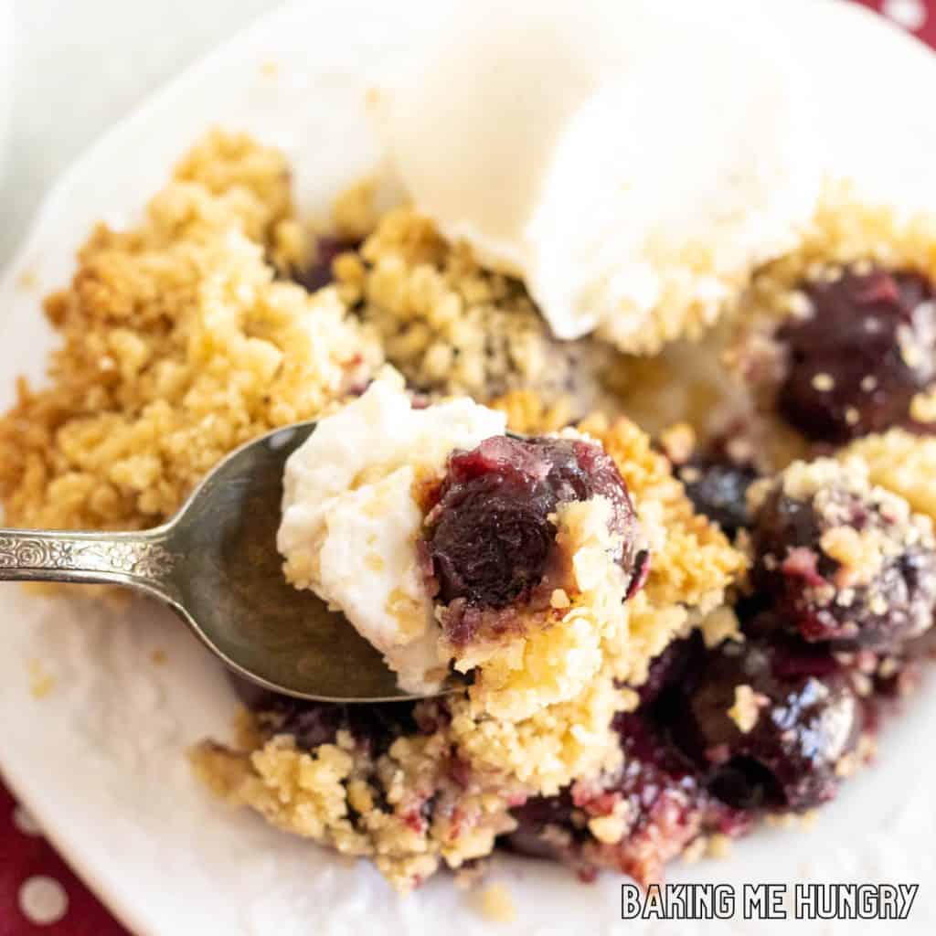 bite of fresh cherry crumble recipe and vanilla ice cream on a spoon resting on plate