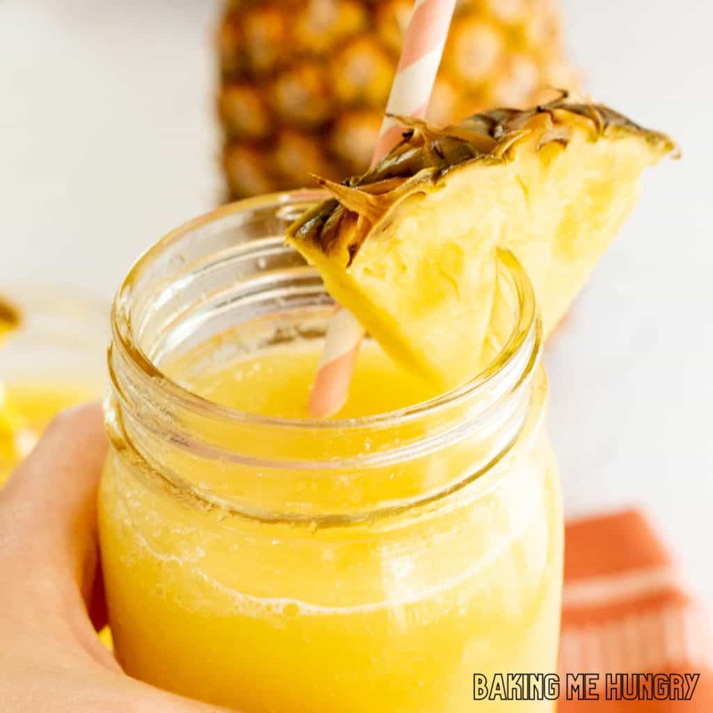 pineapple slushy recipe held up by hand in glass jar with straw and pineapple wedge
