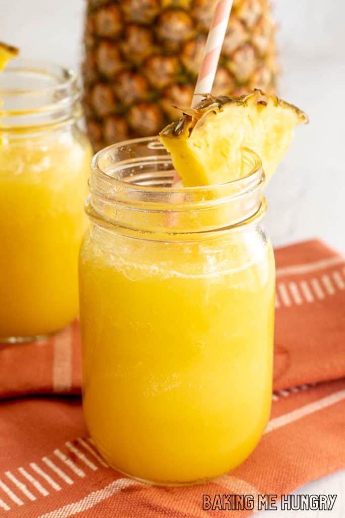 pineapple slushy recipe in glass jar with straw and pineapple wedge
