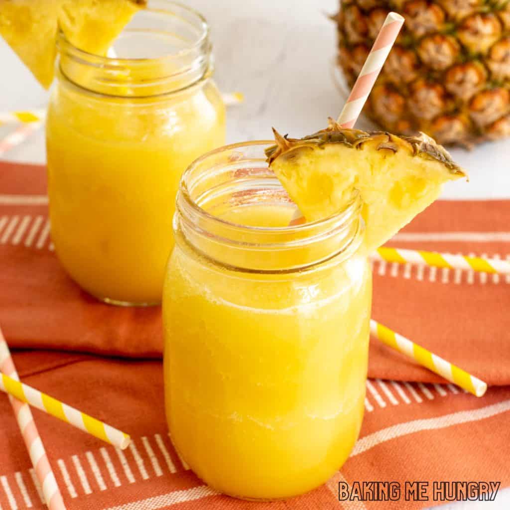 pineapple slushy recipe close up in two mason jars with straws and pineapple wedges as garnish