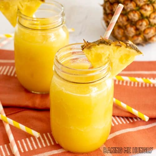 pineapple slushy recipe close up in two mason jars with straws and pineapple wedges as garnish