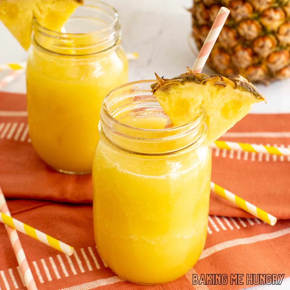 pineapple slushy recipe close up in two mason jars with straws and pineapple wedges as garnish