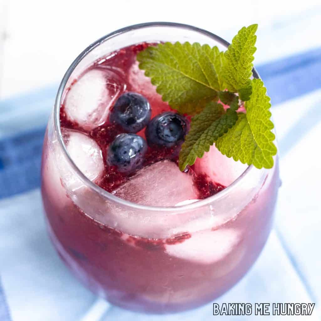 blueberry mocktail in stemless wine glass on a blue napkin with mint and blueberries as garnish