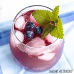 blueberry mocktail in stemless wine glass on a blue napkin with mint and blueberries as garnish