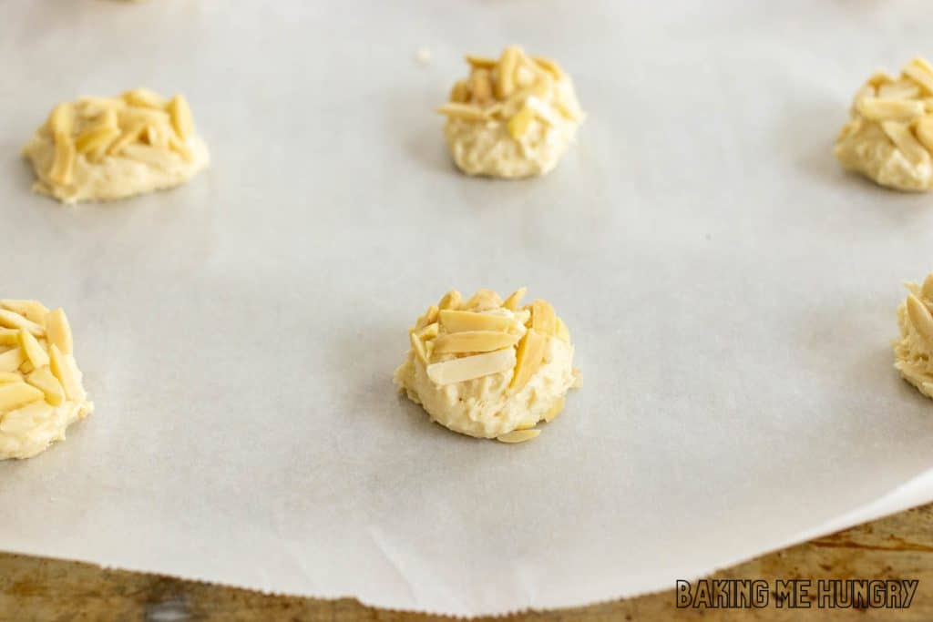 balls of cookie dough with slivered almonds pressed on top on baking sheet with parchment