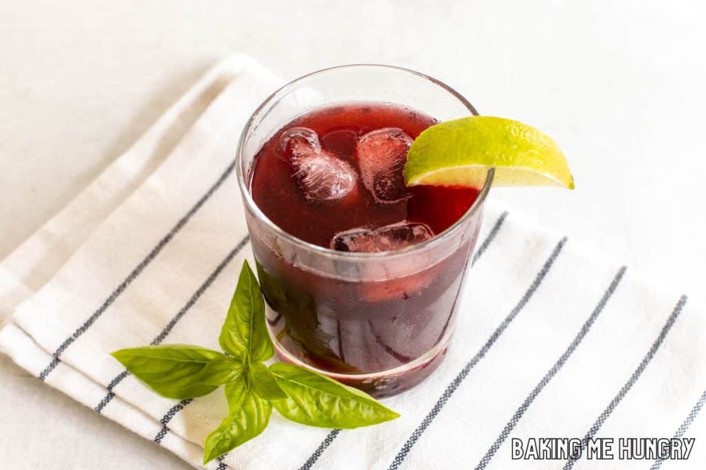 blackberry mocktail in glass with lime wedge and basil garnish on striped napkin