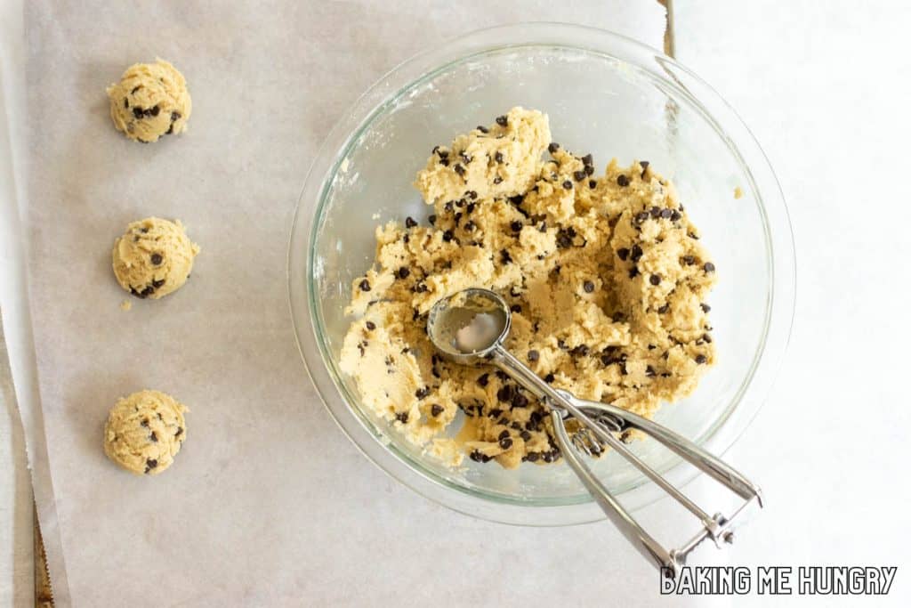 cookie scoop in mixing bowl next to tray with balls of dough