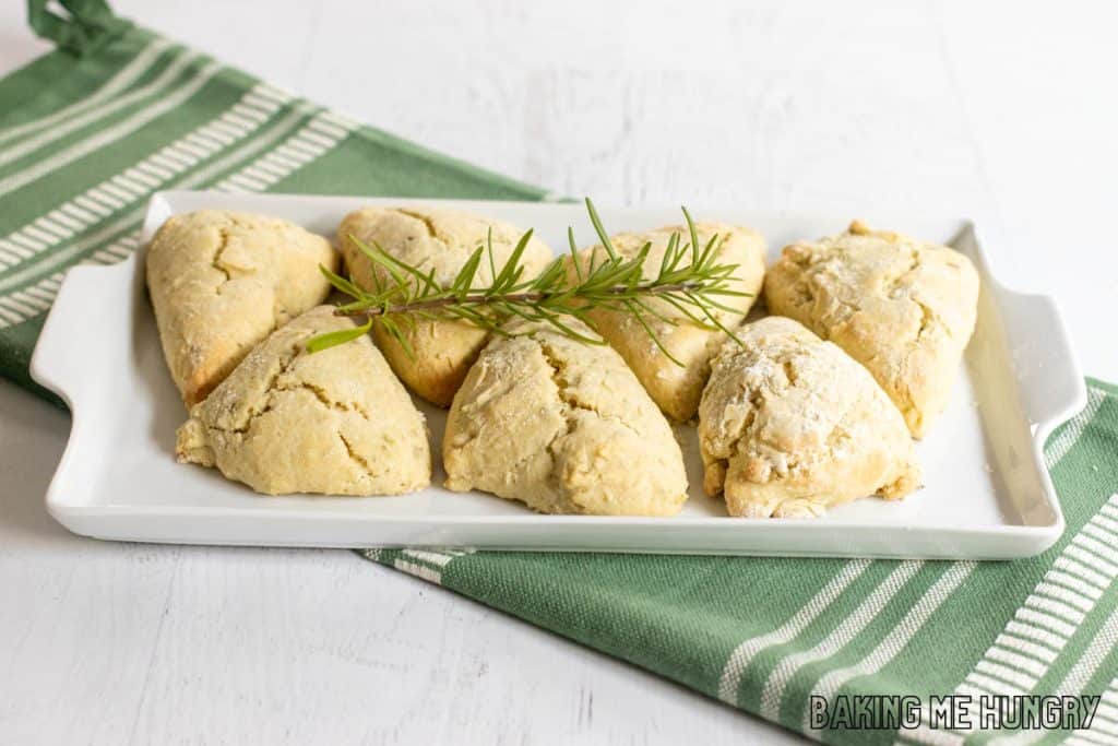 Fresh herb scones on a white platter with rosemary garnish.