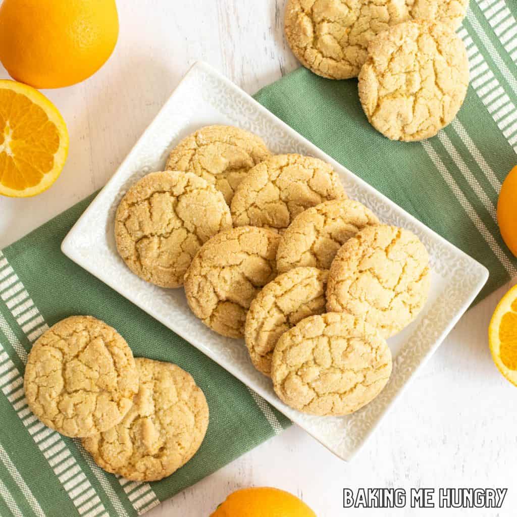 orange sugar cookies on serving platter with green towel and orange fruits around