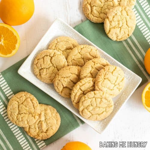 orange sugar cookies on serving platter with green towel and orange fruits around