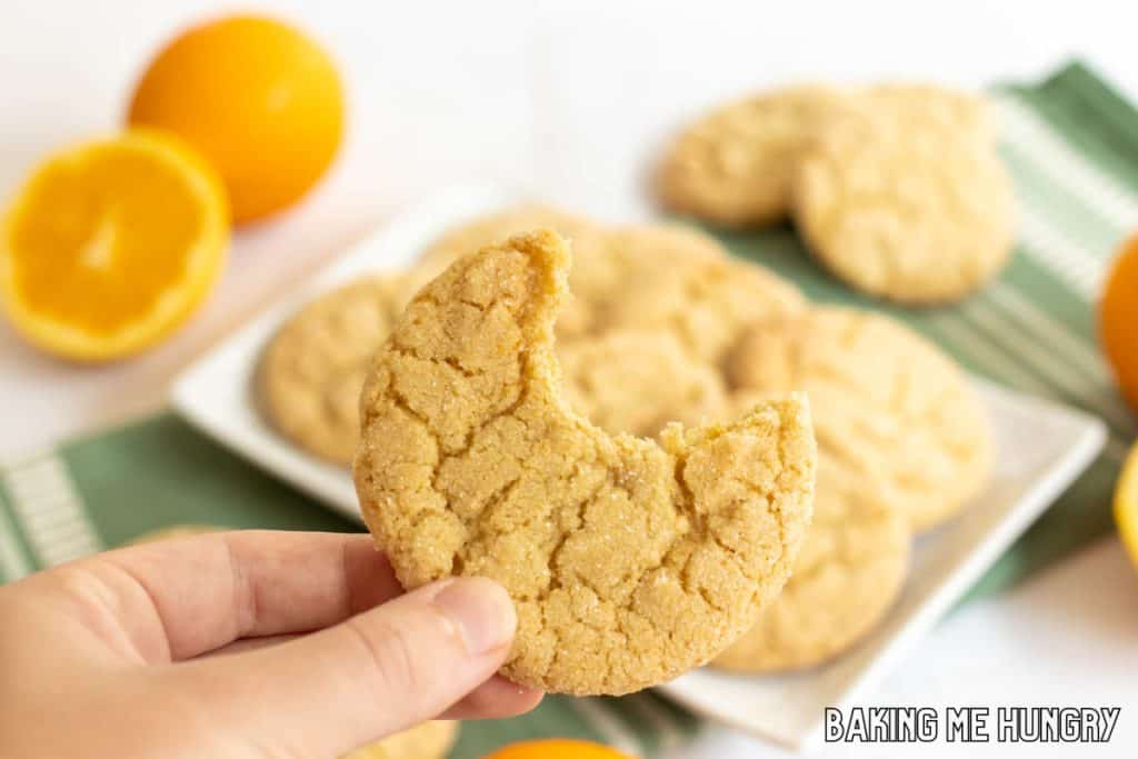 hand holding up an orange sugar cookie missing a bite